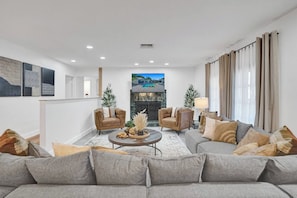 A modern living room with a grey sofa, two leather armchairs, a coffee table, and a fireplace. - Family villa w/ heated pool, gameroom & fire pit (Davie)