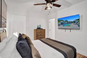 A bedroom with a bed, a ceiling fan, a dresser, and a TV displaying a pool view. - Family villa w/ heated pool, gameroom & fire pit (Davie)