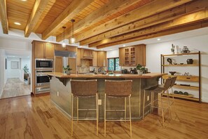 A modern kitchen with wooden beams, a central island with bar stools, and built-in appliances. - Family villa w/ heated pool, gameroom & fire pit (Davie)