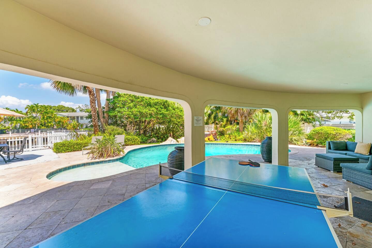 A pool table in a covered area with a view of a swimming pool and outdoor furniture.