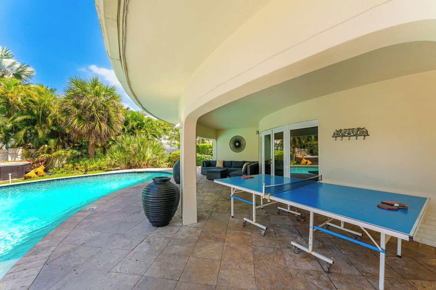Un espace aménagé au bord de la piscine, comprenant une table de ping-pong, des sièges d’extérieur et une vue sur la piscine.