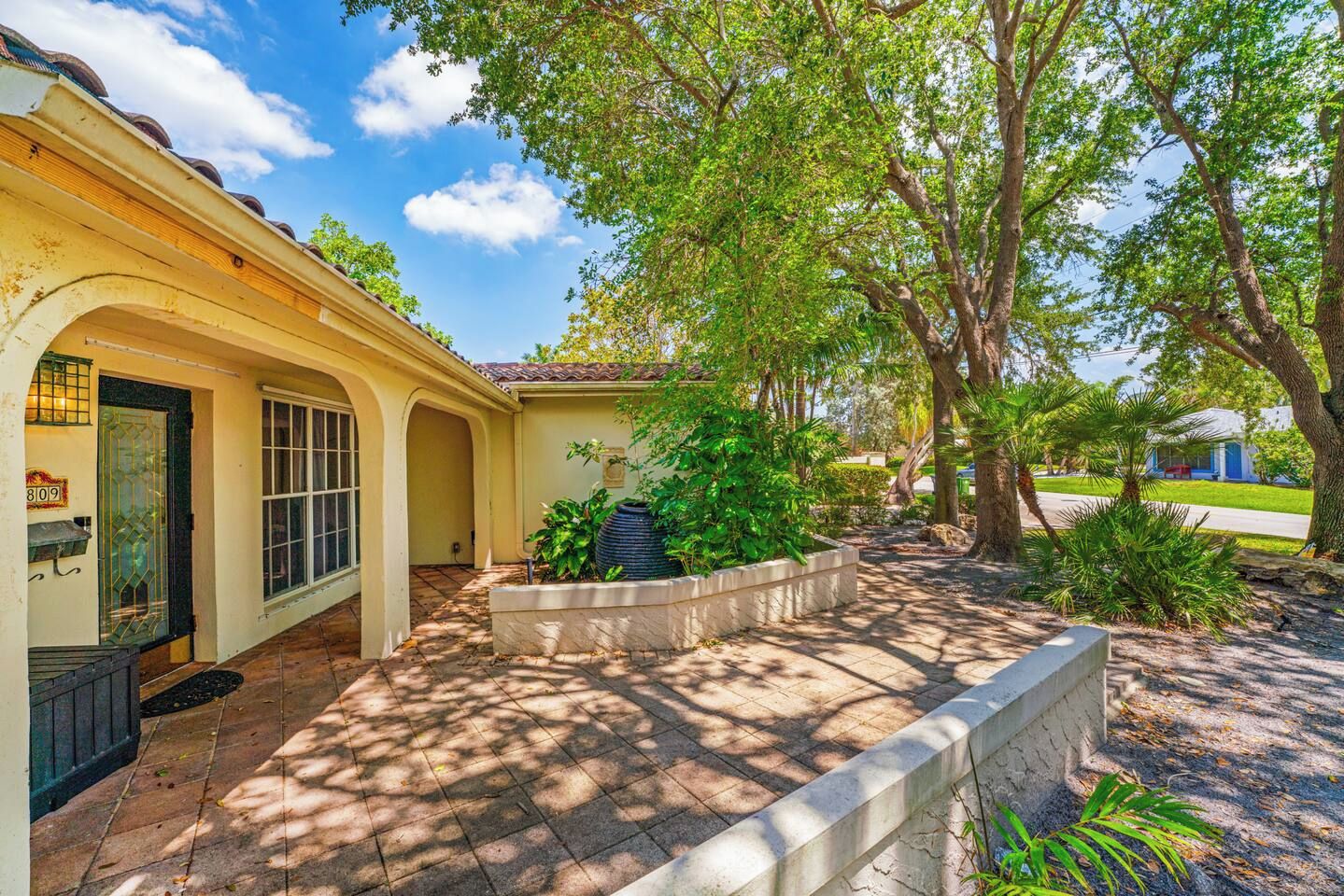 A residential property with a covered patio, a large tree, and a well-maintained garden.