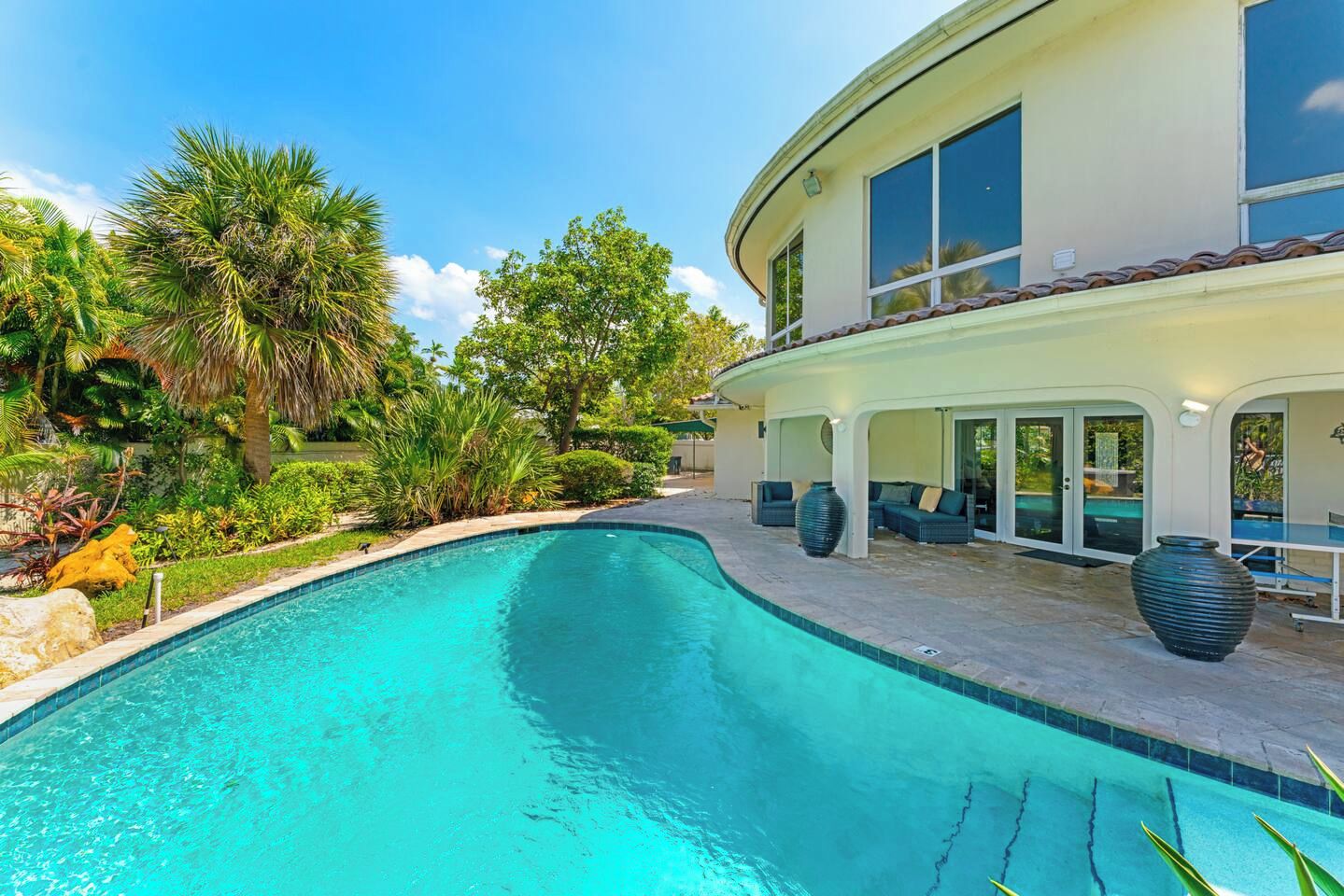 A swimming pool with a curved edge, surrounded by a patio area with outdoor furniture and a covered seating area.