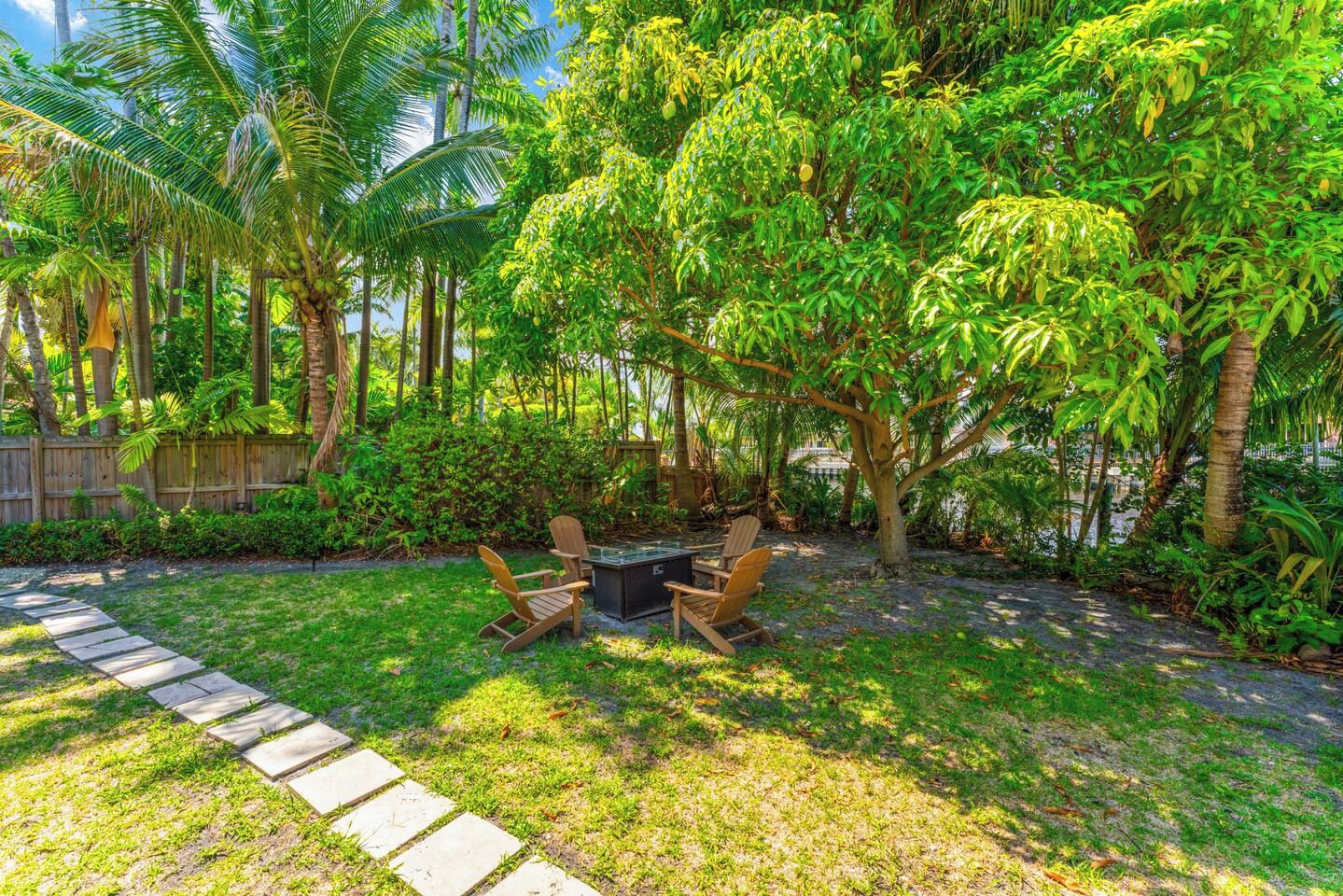 A garden with a stone pathway, a wooden table with chairs, and various tropical plants.
