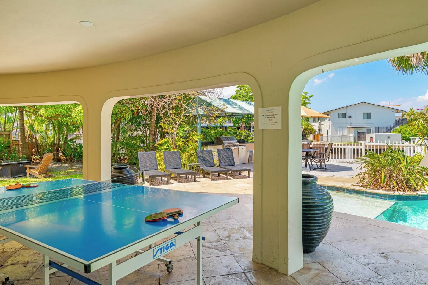 An outdoor pool area with a table tennis table, lounge chairs, and a view of a residential building.
