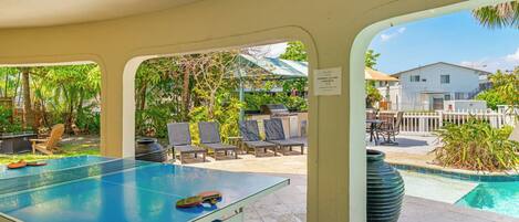 An outdoor pool area with a table tennis table, lounge chairs, and a view of a residential building.