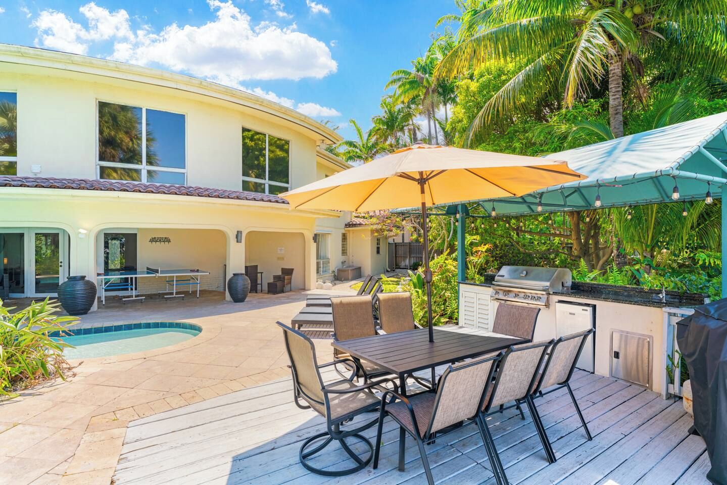 A poolside area with a table and chairs, a barbecue grill, and a covered patio.