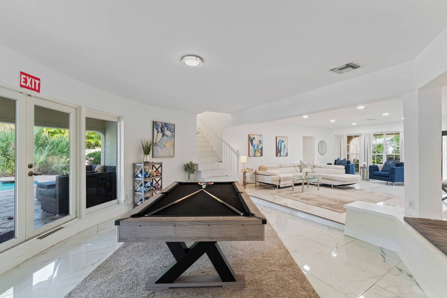 A modern indoor pool area with a pool table, a staircase, and a seating area with sofas and a coffee table.