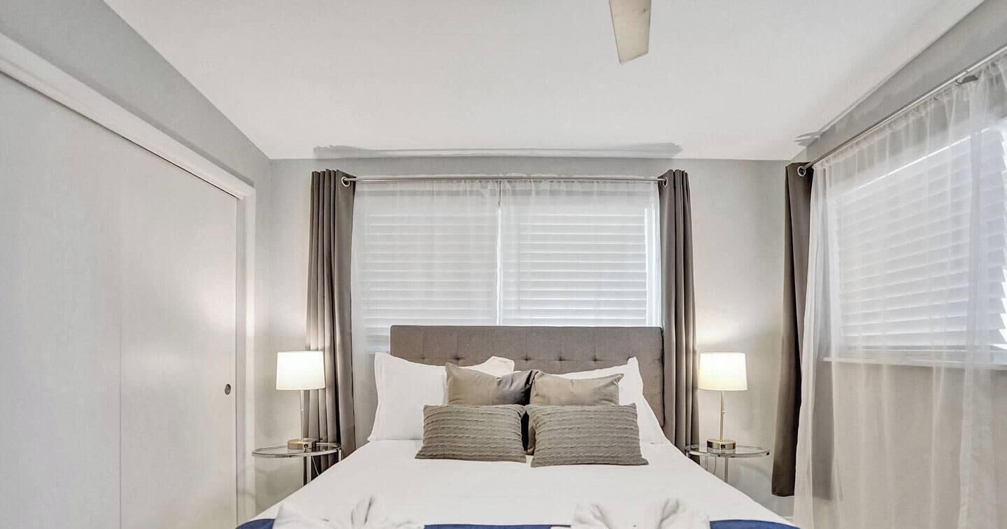 Een hotelkamer met een groot bed, twee nachtkastjes met lampen, een plafondventilator en een raam met gordijnen.