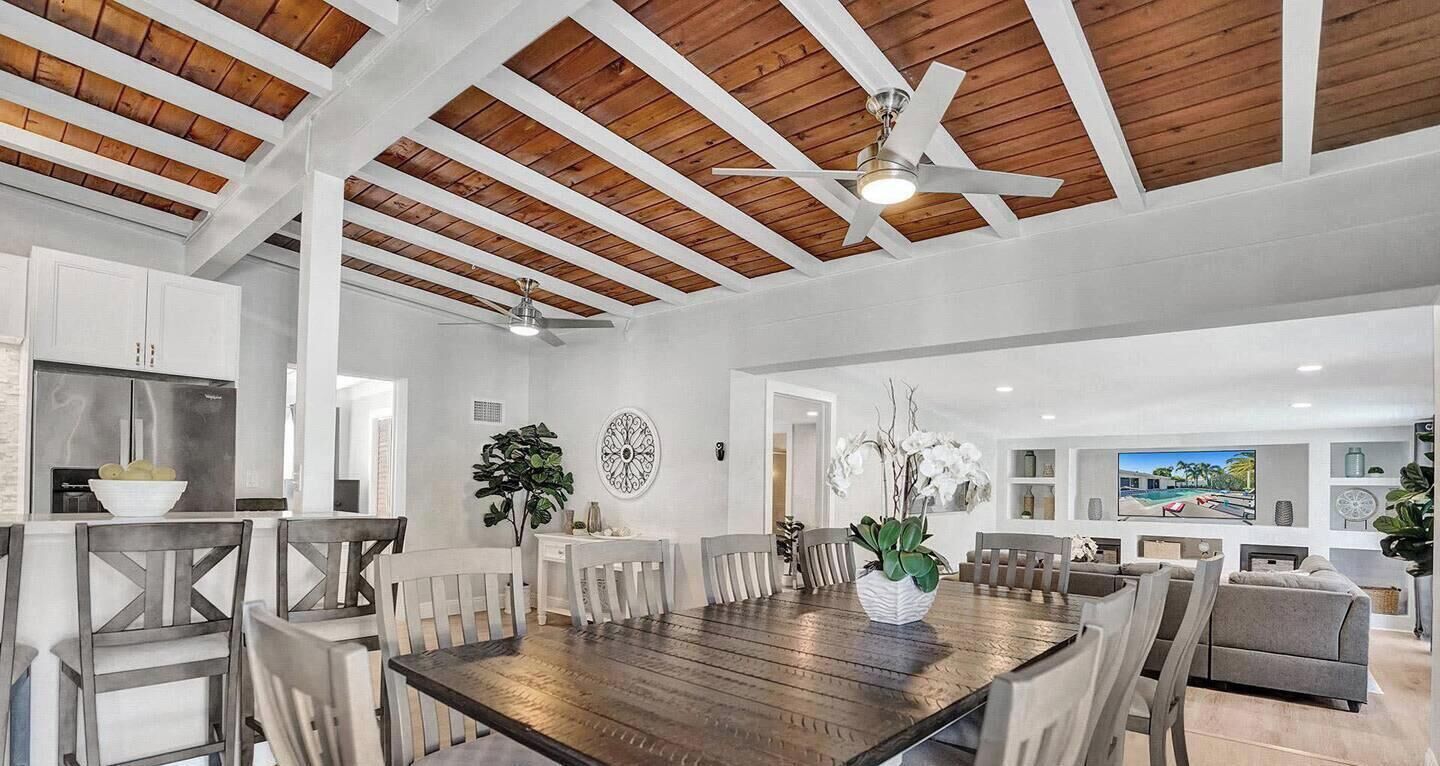 A spacious dining area with a wooden table and chairs, a ceiling fan, and a view of the living room.