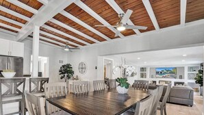 Un vaste espace dédié à la salle à manger, avec une table et des chaises en bois, un ventilateur de plafond et une vue sur le salon.