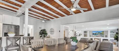 A spacious dining area with a wooden table and chairs, a ceiling fan, and a view of the living room.