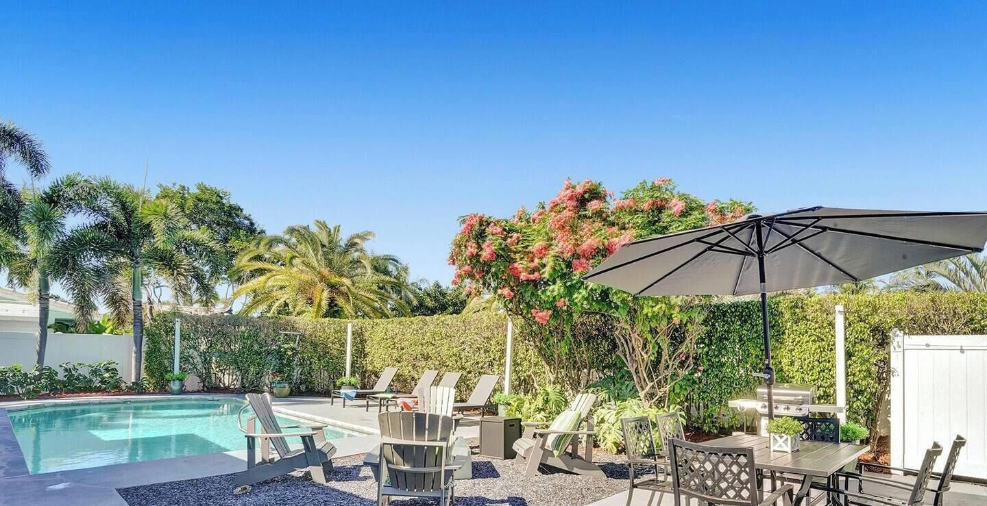 Un espace piscine aménagé avec des chaises longues, un barbecue et une pergola dotée d’un auvent.