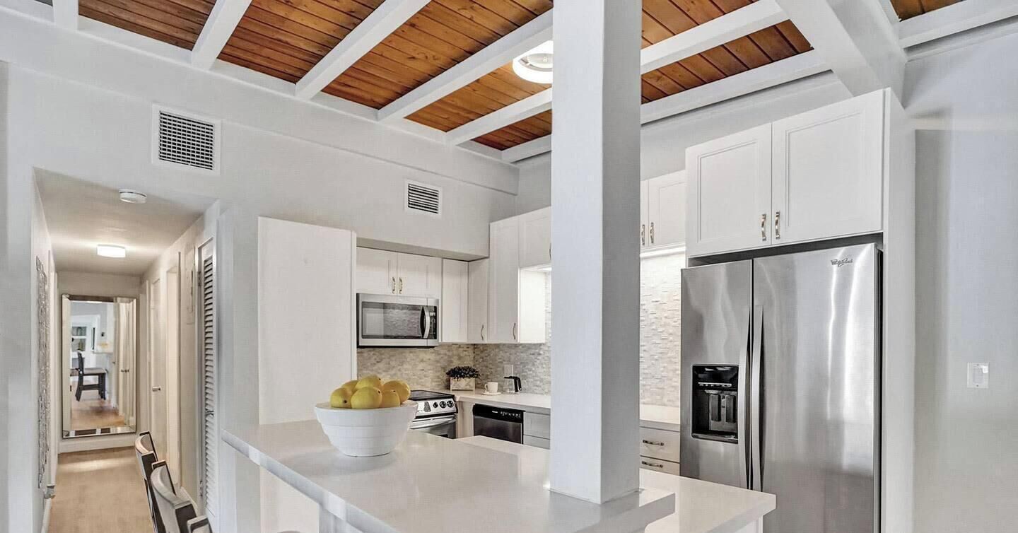 A modern kitchen with white cabinetry, a stainless steel refrigerator, and a central island with a bowl of fruit.