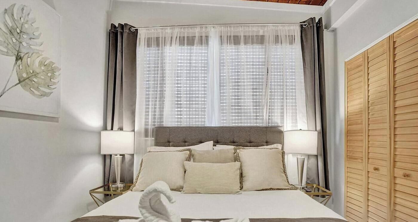 Une chambre d’hôtel avec un grand lit, deux lampes de chevet, une fenêtre avec des rideaux légers et une armoire en bois.