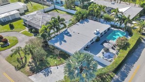 Vue aérienne d’un quartier résidentiel avec une piscine, entourée de palmiers et d’une pelouse bien entretenue.