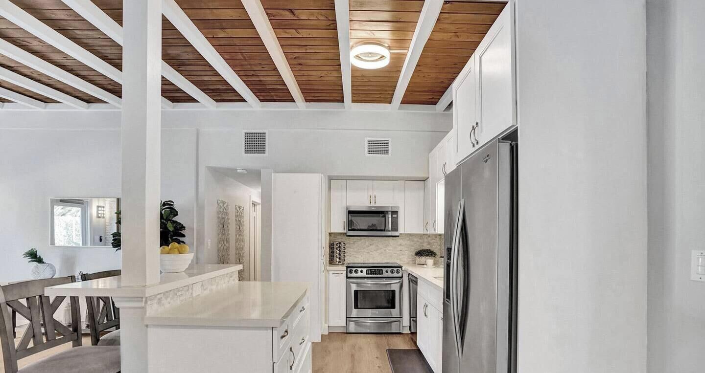 Una cocina moderna con armarios blancos, electrodomésticos de acero inoxidable y techo de madera.