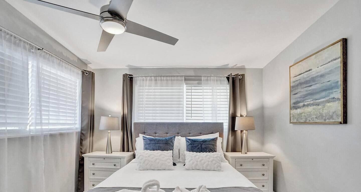 A bedroom with a bed, bedside tables, a ceiling fan, and a painting on the wall.