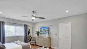 A hotel room with a bed, a ceiling fan, a dresser, a door, and a window with curtains.
