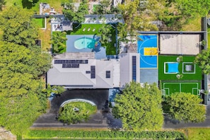 An aerial view of a property with a swimming pool, basketball court, and a covered area with seating.