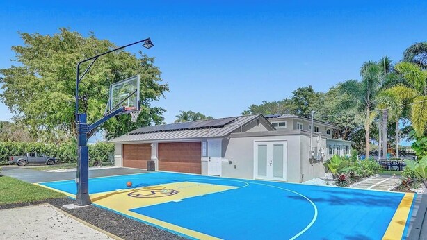 A basketball court with a hoop, a small building, and surrounding greenery.