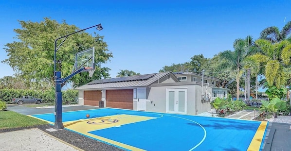 A basketball court with a hoop, a small building, and surrounding greenery.
