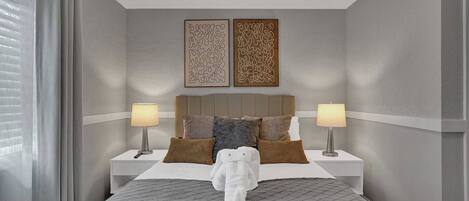 A hotel room with a bed, two bedside lamps, a headboard, and two wall art pieces.