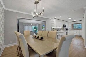 Una cocina moderna con armarios blancos, una isla central y un comedor con mesa y sillas de madera.