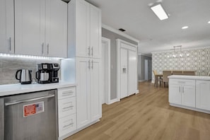 A modern kitchen with white cabinets, a stainless steel refrigerator, and a coffee maker.