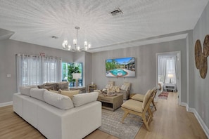 A modern living room with a white sofa, a coffee table, and a TV displaying a pool view.