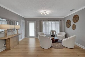 A modern living room with a wooden floor, a white sofa set, a coffee table, and decorative wall art.