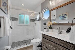 Un baño moderno con cabina de ducha de vidrio, inodoro, lavamanos con tocador de madera y un espejo grande.