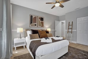 A hotel room with a bed, bedside tables, a ceiling fan, artwork on the wall, and a wardrobe.