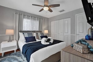 A bedroom with a bed, nightstands, a ceiling fan, a window with curtains, and a dresser with decorative items.