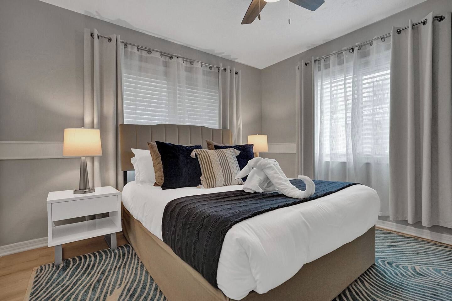 Een hotelkamer met een bed, nachtkastjes, een plafondventilator en een raam met gordijnen.