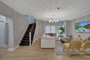 Una sala de estar moderna con una escalera, un sofá blanco, una mesa de centro y un televisor en la pared.