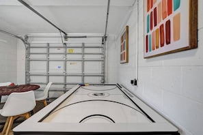 A room with a shuffleboard table, chairs, and a wall-mounted rack. - Modern house w/ heated pool & game room (Pompano Beach)