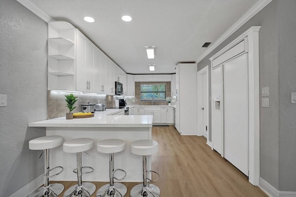 A modern kitchen with white cabinetry, a central island with bar stools, and a window providing natural light.