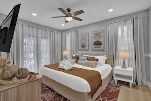 Una habitación de hotel con cama, televisor, ventilador de techo y obras de arte en las paredes.
