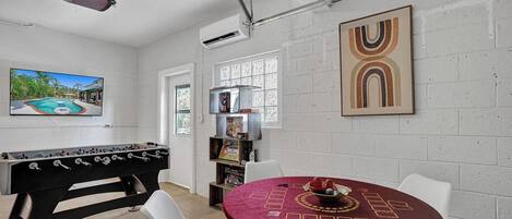 Ein Zimmer mit Billardtisch, Kicker, Esstisch mit Poker-Set und einem großen abstrakten Gemälde an der Wand.