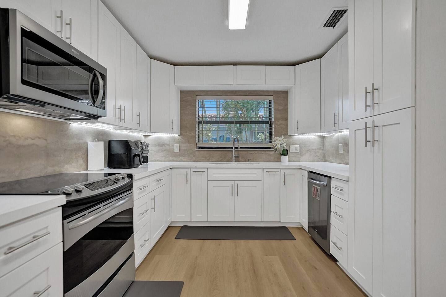 Una cucina moderna con mobili bianchi, forno a microonde integrato, piano cottura e lavastoviglie.