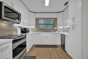 Una cocina moderna con armarios blancos, microondas integrado, estufa y lavavajillas.