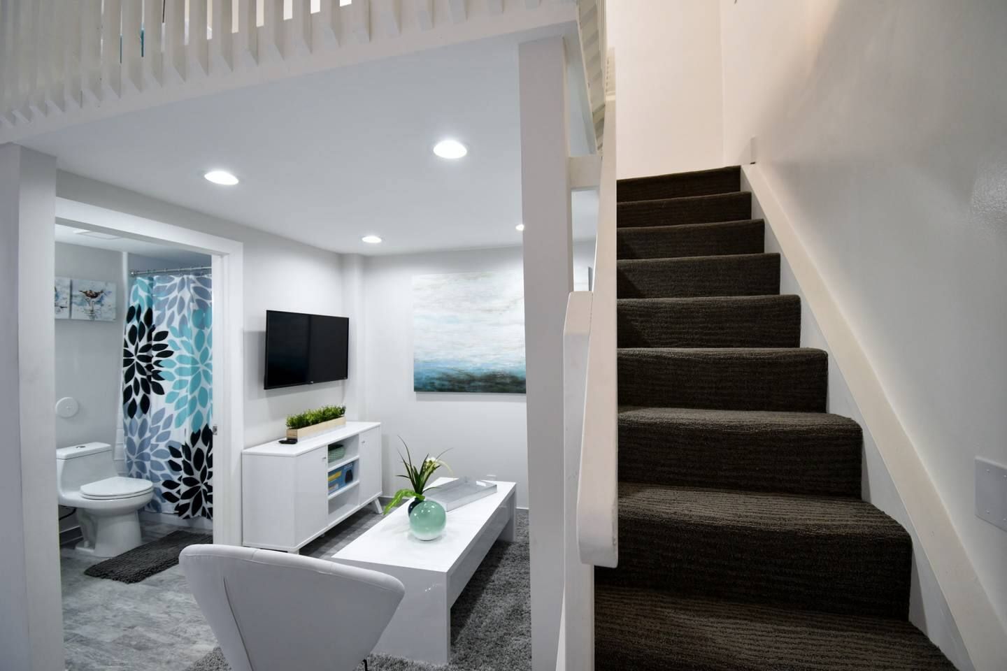 A modern interior with a staircase, a flat-screen TV, a white console, and a painting on the wall.