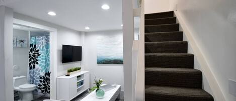 A modern interior with a staircase, a flat-screen TV, a white console, and a painting on the wall.