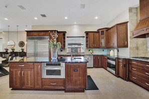 A modern kitchen with a large island, stainless steel appliances, wooden cabinetry, and a dining area with chairs. - Villa w/pool, mini-golf & firepits (Davie)