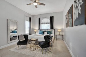 A modern bedroom with a bed, two chairs, a small table, a ceiling fan, and artwork on the walls. - Villa w/pool, mini-golf & firepits (Davie)