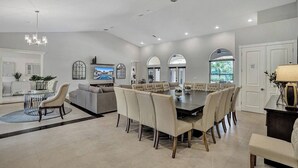 Ein großzügiger Essbereich mit einem großen runden Tisch und Stühlen, ein Küchenbereich mit Einbauofen sowie eine Sitzecke mit Sofas und Fernseher.