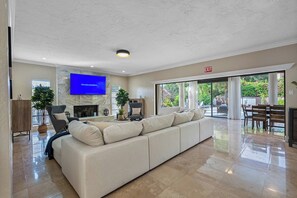 Amplia sala de estar con un sofá modular grande, un televisor de pantalla plana montado en la pared, una chimenea y un comedor con mesa y sillas.
