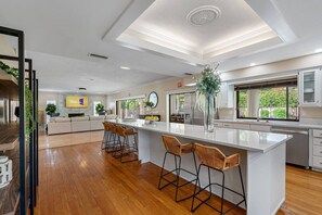 Una cocina moderna con una isla central, taburetes de bar y un ventanal grande.