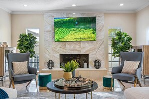 A spacious living room with a large flat-screen TV mounted on a marble wall, two armchairs, a coffee table with decorative items, and a fireplace. - Pool - Soccer - Movie Room - Game Room - Sleeps 20 (Largo)
